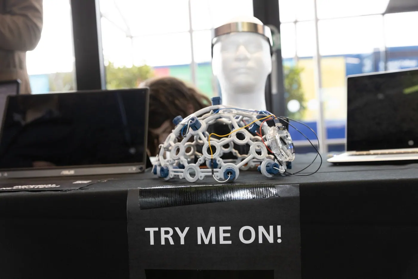 An EEG headset prototype on a mannequin head beside a sign reading Try me on