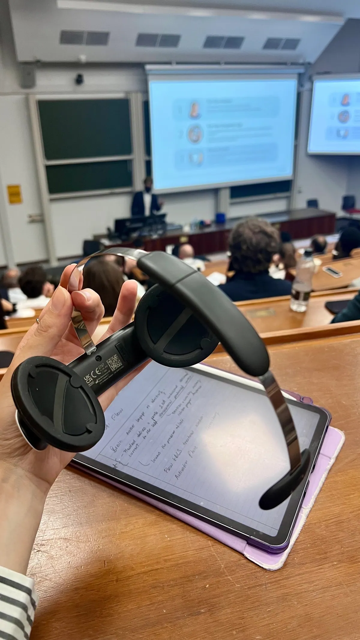 An attendee's notes and a prototype device on a lecture theatre desk