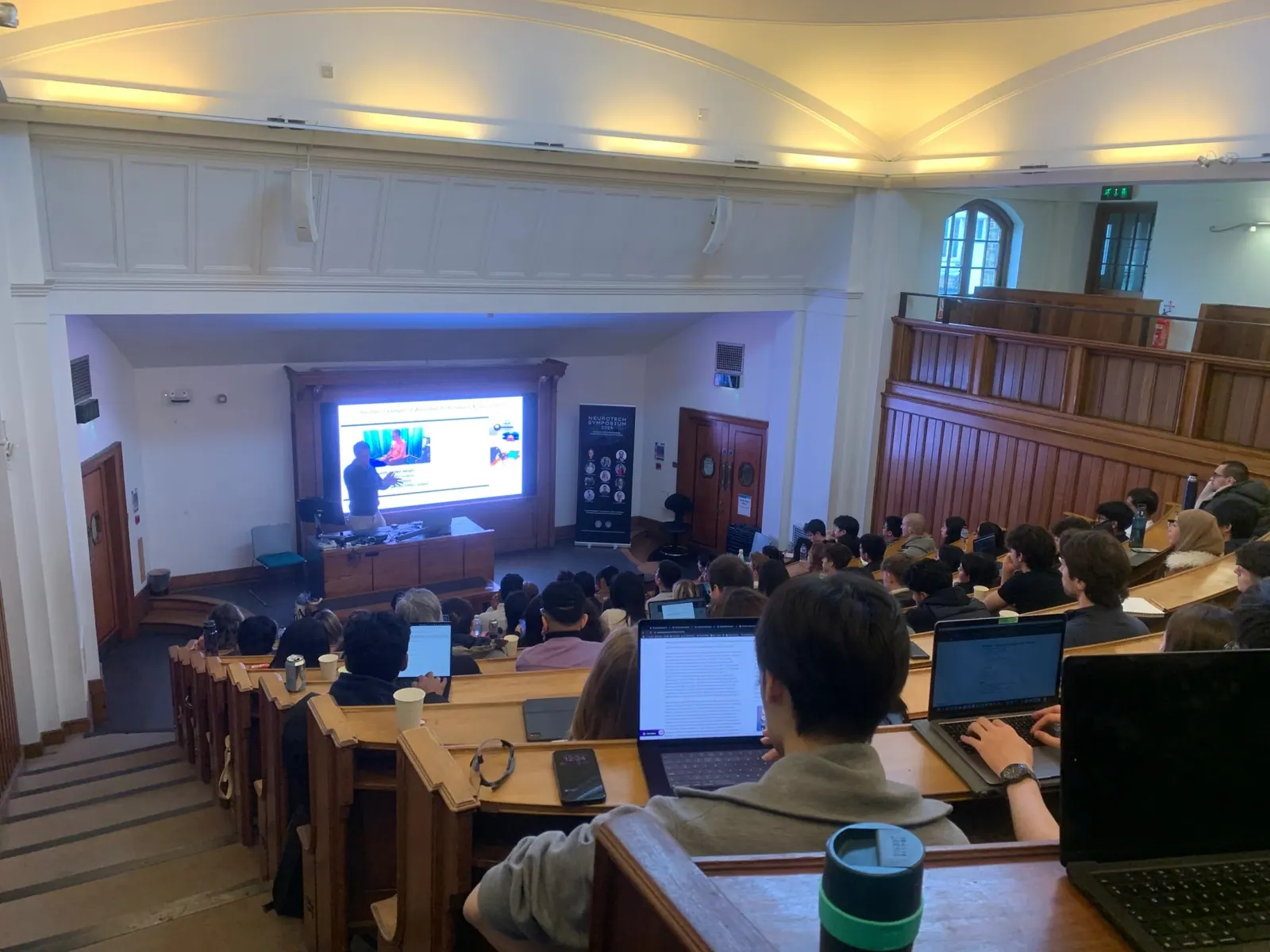 Audience watching a talk in a wood-panelled lecture theatre